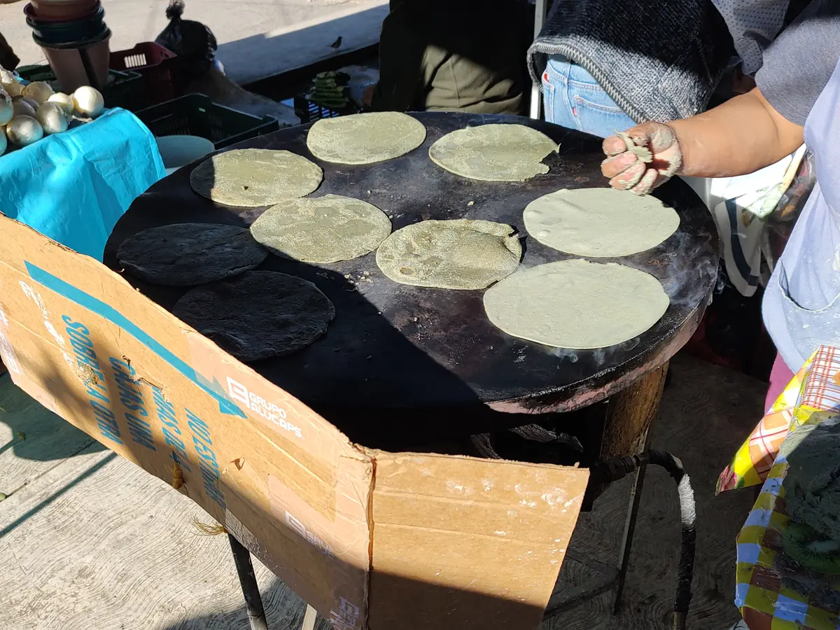 Archival photograph: a cook turns blue-corn tortillas on a wood-fired comal at a street market in Tlaxcala, Mexico.